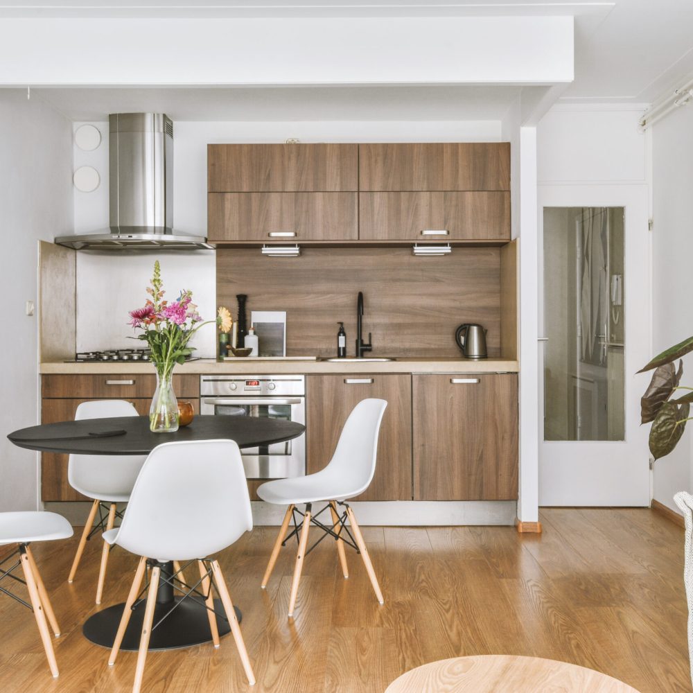Table with chairs and flowers located near lounge area and kitchen in spacious room of contemporary apartment